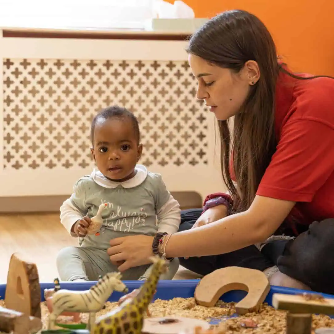 Babies Little girl and caregiver engaging in sensory play with animal toys at Monkey Puzzle Day Nursery Stoke Newington.