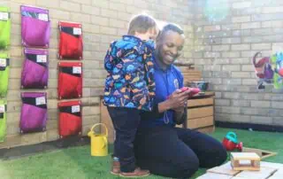 Bright nursery staff and a child engaging with a mobile device at Monkey Puzzle Day Nursery Stoke Newington, showcasing a nurturing environment for early childhood development.
