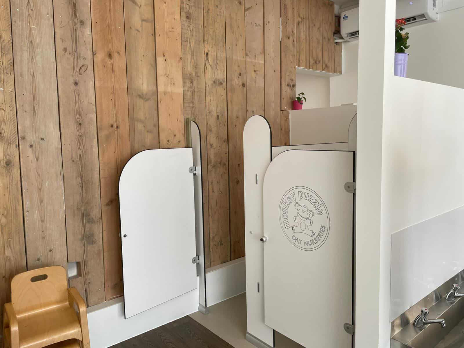 White nursery privacy screens with "Monkey Puzzle Day Nurseries" logo in a modern childcare setting.
