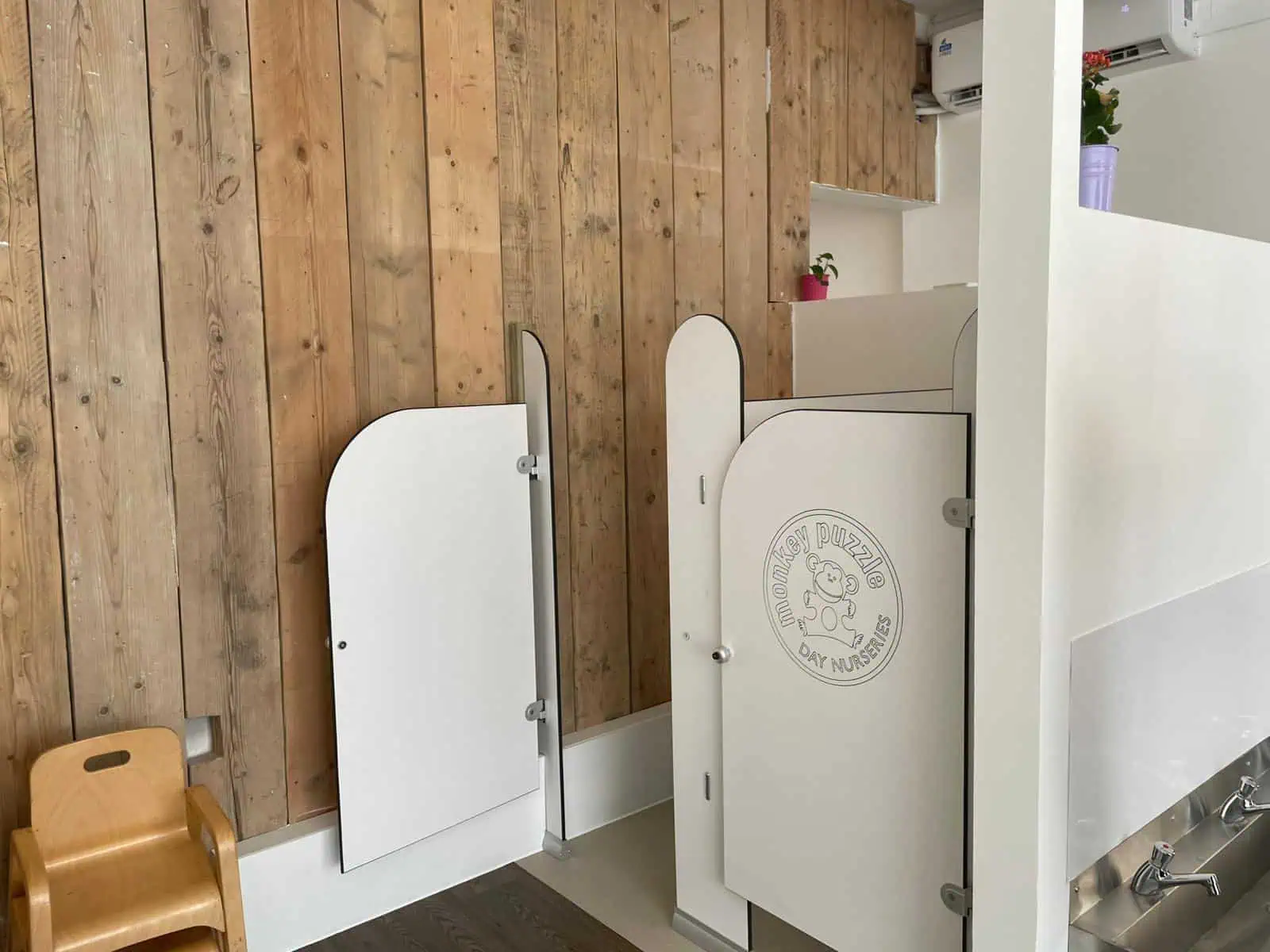 White nursery privacy screens with "Monkey Puzzle Day Nurseries" logo in a modern childcare setting.